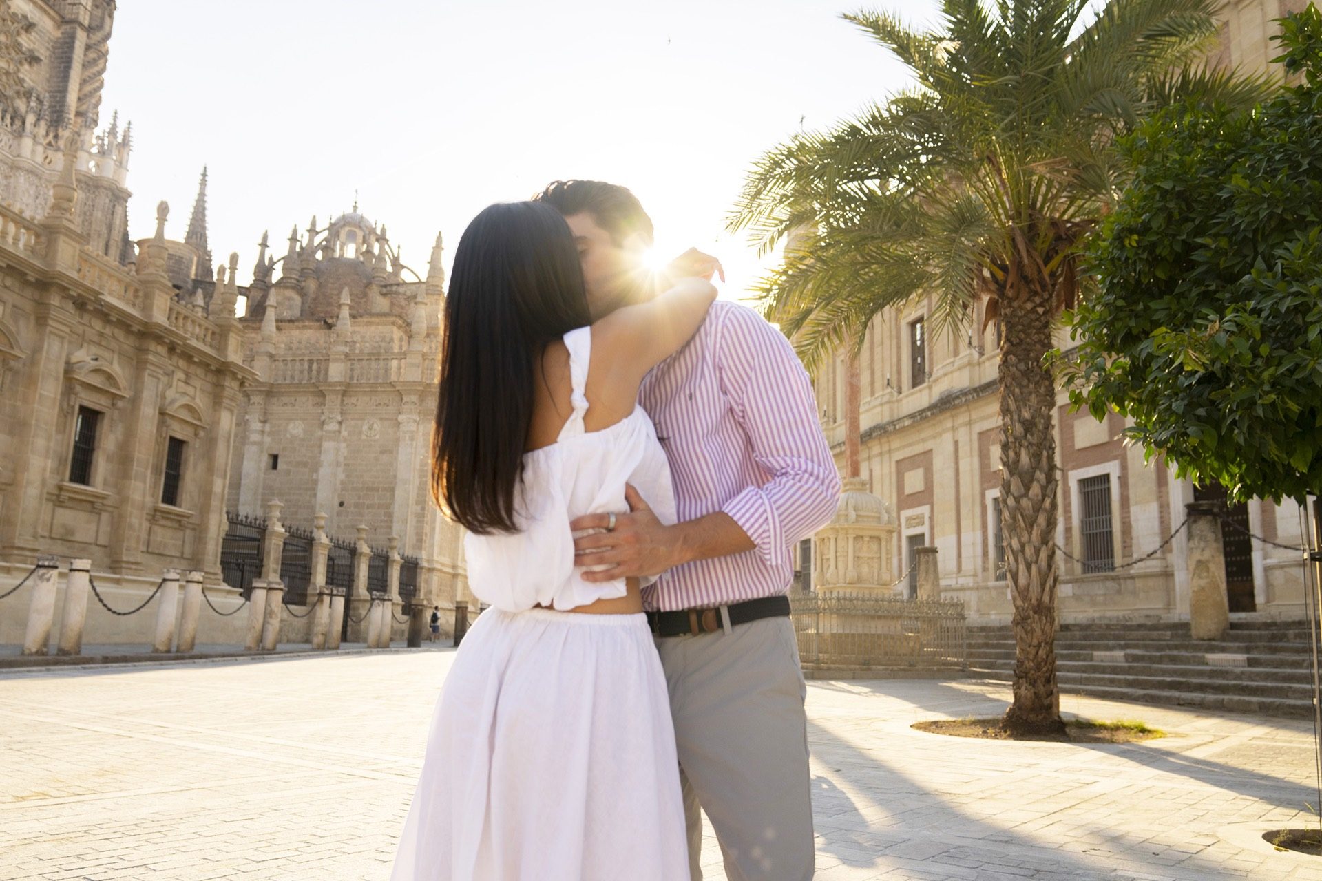 Couple kissing in the sunlight by Seville Cathedral after their proposal